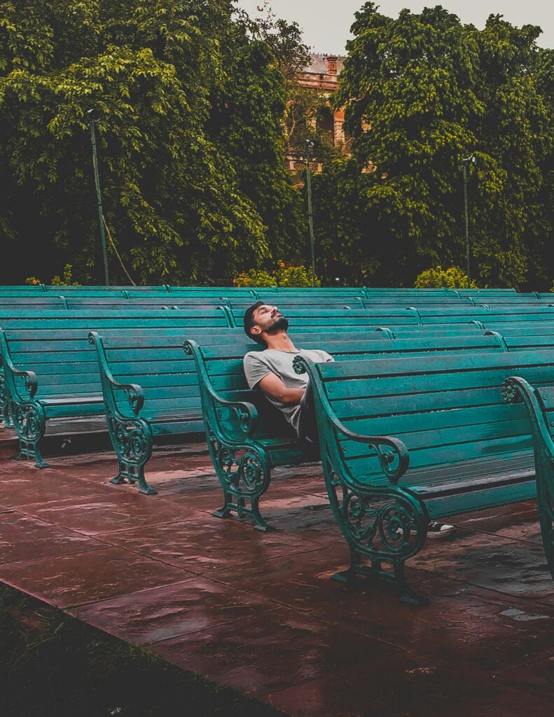 A man enjoys solitude on a series of teal benches in a lush park.