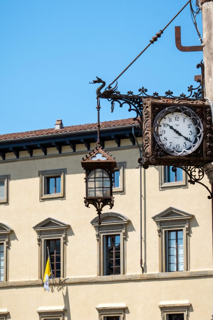 An ornate clock and lantern adorn a historic building facade in Florence, Italy.