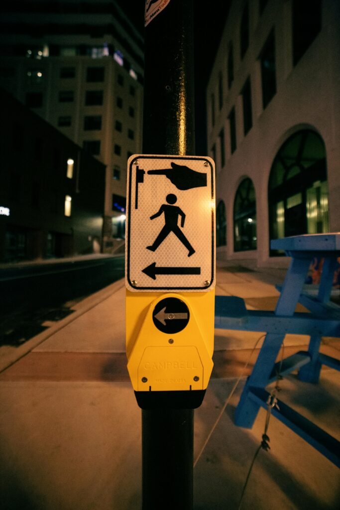 Post with sign for pedestrians showing direction and rule for pressing button before crossing road