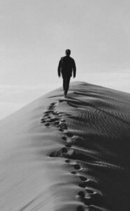 A solitary person walks along the crest of a sand dune, leaving footprints in the desert.