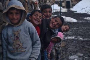 Group of children joyfully posing outdoors in a snowy village setting.