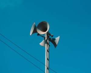 A set of loudspeakers on a pole against a bright blue sky, symbolizing communication and technology.