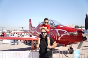 Father and son enjoying a sunny day at the air show in Adana with a red aerobatic plane.