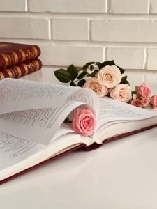 Composition of opened book with delicate pink roses placed on white pages and table in bright room